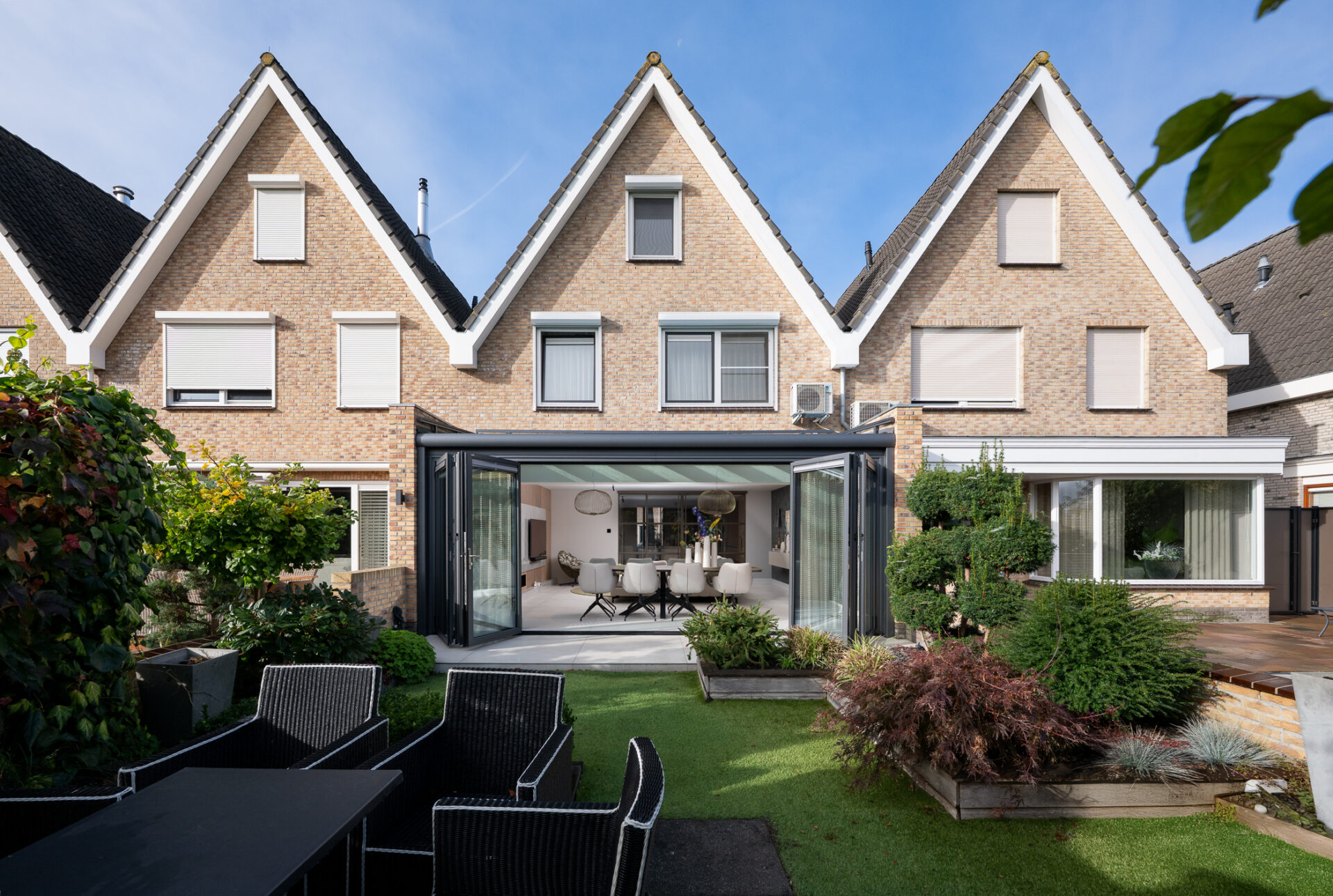 volledig geopende glazen vouwwand met donkere profielen aan een woninguitbouw met doorgang naar de tuin